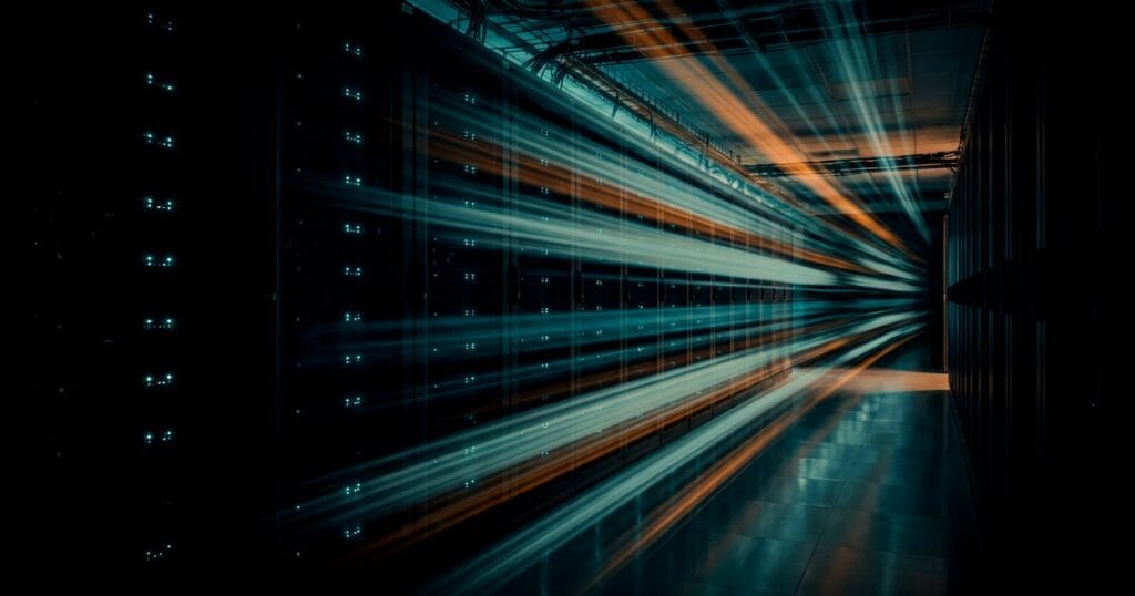 Long-exposure teal and orange light trails racing down a dark server-rack corridor toward a vanishing point on the right, for a guide to speeding up WordPress for Arabic sites.