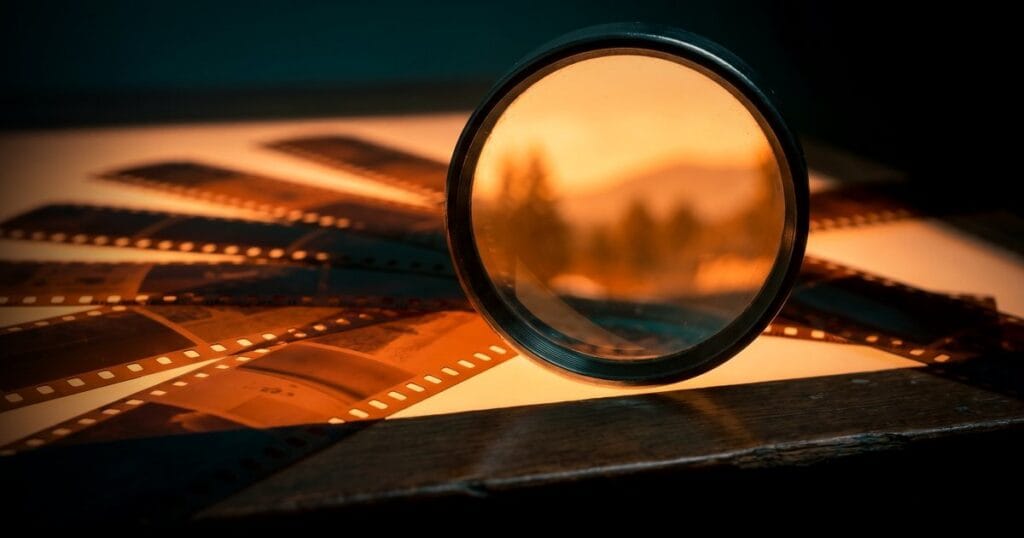عدسة مكبرة فوق شرائط أفلام على طاولة إضاءة كهرمانية، تعبيرًا عن تحسين الصور وتسريع موقع ووردبريس.