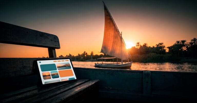 A tablet showing a travel-booking website layout rests on a weathered wooden boat bench while a felucca's sail glows orange at sunset on the Nile, for choosing a WordPress travel agency theme.